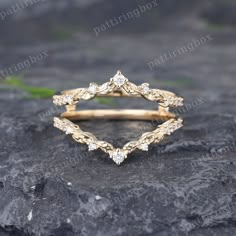 a gold wedding ring with diamonds on top of a stone slab in front of some grass