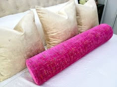 a bed with three pillows on it and a pink pillow in front of the headboard