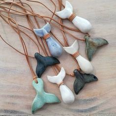 several sea glass birds are hanging from a string on a wooden table with brown leather cord