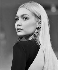 a woman with long blonde hair and earrings on her neck looking off to the side