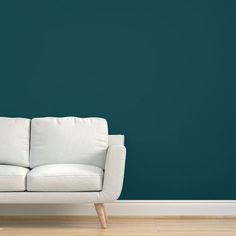 a white couch against a teal green wall in an empty room with wooden floors