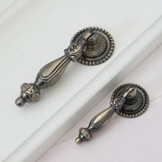 two silver handles on a white cabinet with bead trimmings and knobs