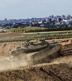 an army tank driving down a dirt road in front of a large city with tall buildings