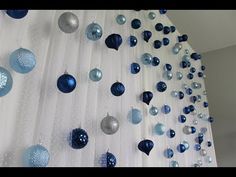 blue and silver ornaments are hanging from the ceiling in front of a white curtain with polka dots