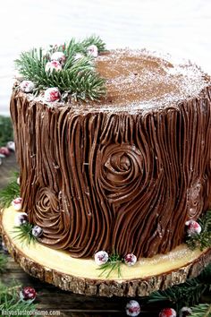 a chocolate cake with frosting and pine sprigs on top is sitting on a tree stump