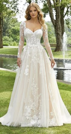 a woman in a wedding dress standing on grass with trees and water behind her, posing for the camera