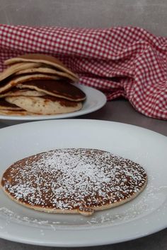 two plates with pancakes on them and a red checkered table cloth in the background