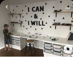 a young boy standing in front of a white desk with black letters on the wall