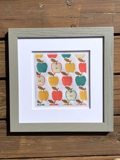 an apple print in a frame on a wooden surface with the background painted white and gray