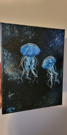 a person holding up a painting with two blue jellyfishs on it's sides