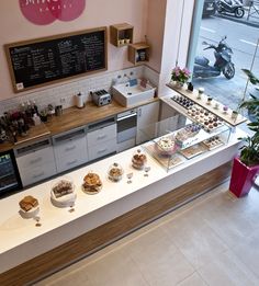 a counter with many desserts on it in front of a window and a motorcycle parked outside the window