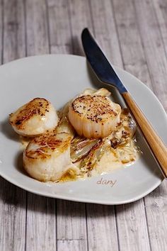 some scallops are sitting on a white plate next to a knife and fork