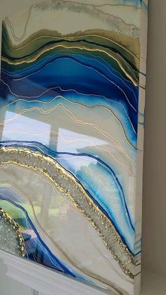 an abstract painting with blue, white and gold colors on the glass window sill