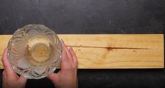 a person holding a glass bowl in front of a piece of wood