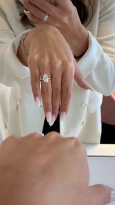 a woman in a white jacket is pointing at her engagement ring on another person's finger