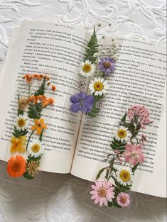 three bookmarks with flowers on them sitting on top of an open book in the shape of letters