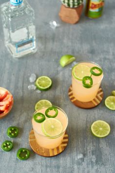 two glasses filled with drinks sitting on top of a table next to sliced limes