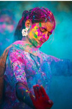 a woman is covered in colored powder and holding her hands out to the side,