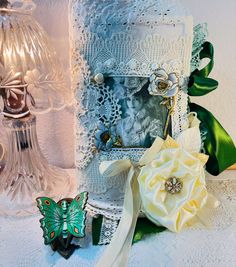 two glass vases with flowers on them next to a lace doily and ribbon