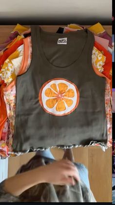 a woman holding up a shirt with an orange design on it