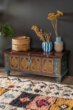 a wooden table topped with vases filled with flowers next to a rug and potted plants