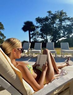 a woman laying on top of a beach chair next to a pool reading a book