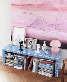 a blue table topped with books and vases next to a painting on the wall