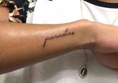 a person with a tattoo on their arm that says paradise in cursive writing