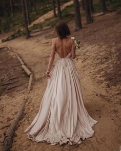 a woman in a long dress walking through the woods with her back to the camera