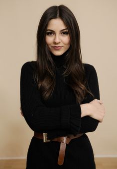 a woman with her arms crossed standing in front of a wall wearing a black sweater dress