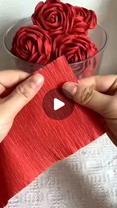 someone is making red roses out of paper in a glass bowl on top of a white towel