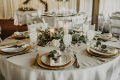 the table is set with silver and gold plates, napkins, candles and greenery