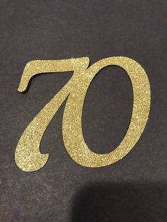 the number seventy is made out of gold glitter and sits on a black table top