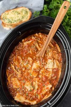 a crock pot filled with pasta and meat in tomato sauce next to garlic bread