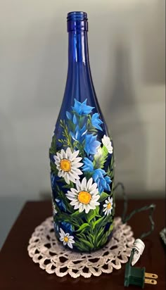 a blue vase with white and yellow flowers painted on it sitting on a doily