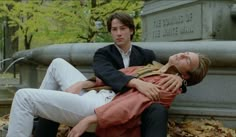 two people laying on the ground in front of a fountain and one person holding his head