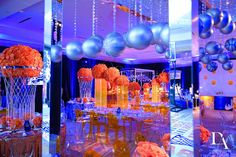 the tables and chairs are set up with orange flowers, silver balls, and blue lights