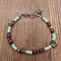 a beaded bracelet with green and red beads on a wooden surface, sitting on top of a table