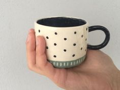 a hand holding a black and white coffee cup with polka dot designs on it's side