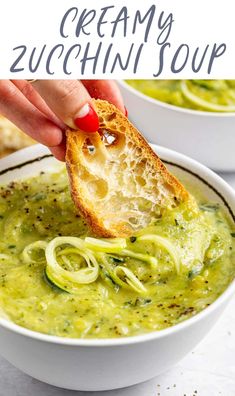 a hand dipping some bread into a bowl of creamy zucchini soup