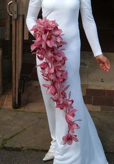 a woman wearing a white dress with pink flowers on the side and long sleeves, standing in front of a door