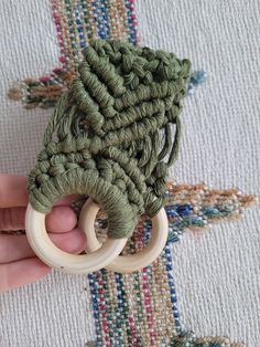 a hand holding a wooden ring with green yarn on it and an elephant toy in the middle