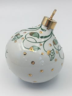 an ornament with gold and green designs on it's side, sitting on a white surface