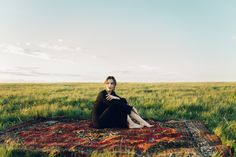 a woman sitting on top of a rug in a field