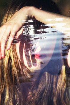 a woman's reflection in the water with her hands on her head and face