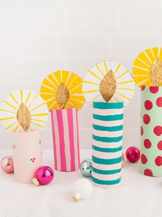 three colorful vases with paper flowers in them on a white tablecloth next to ornaments