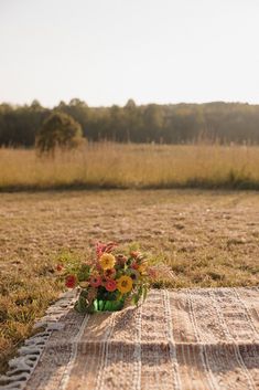 a vase filled with flowers sitting on top of a rug in the middle of a field