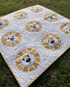 a yellow and white quilt with lions on it in the middle of some green grass