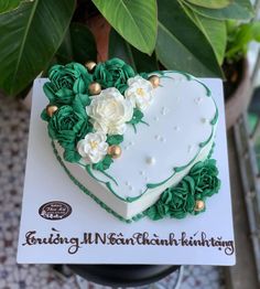 a heart shaped cake with green and white icing on a card next to a potted plant