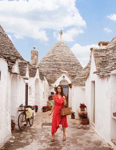 a woman in a red dress is walking through an alley way with white buildings and bicycles